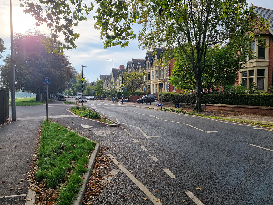 A photograph showing the beginning of the cycle track on the carriage way, that joins onto a shared surface at the Ninan Road/ Alder Road junction, with the zebra parallel cycle crossing in the background.