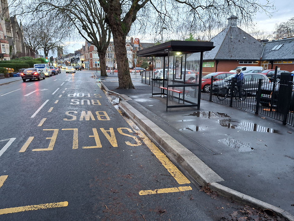 A photograph showing in the foreground a relocated bus stop and shelter on Pen-Y-Lan Road, near the entrance to the car park, which is shown in the background.