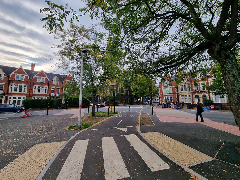 A photograph showing a pedestrian zebra crossing over a bi-directional cycle track in the foreground, and several signalised crossings in the background, at the Ninan Road, Pen-Y-Lan Road, Marlborough Road and Wellfield Road junction.