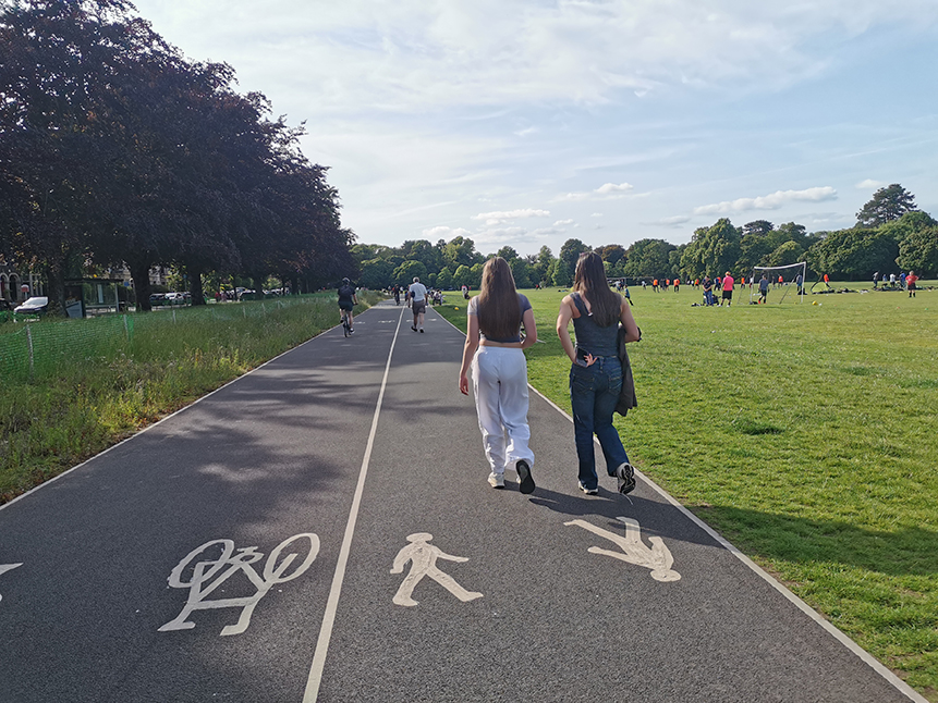 A photograph showing pedestrians waling on the footpath in the foreground and cyclist cycling on the cycle track in the background at Roath Recreational Grounds.