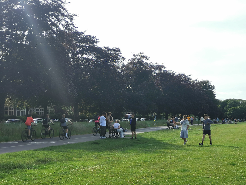 A photograph showing groups of youth at the Roath Recreational Grounds, using the new benches in the foreground and four youth cyclists using the cycle track in the background.